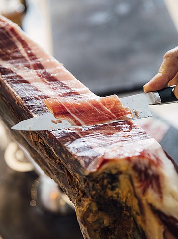 Nahaufnahme des Aufschneidens von haundünnen Scheiben eines Stücks Jamón Ibérico